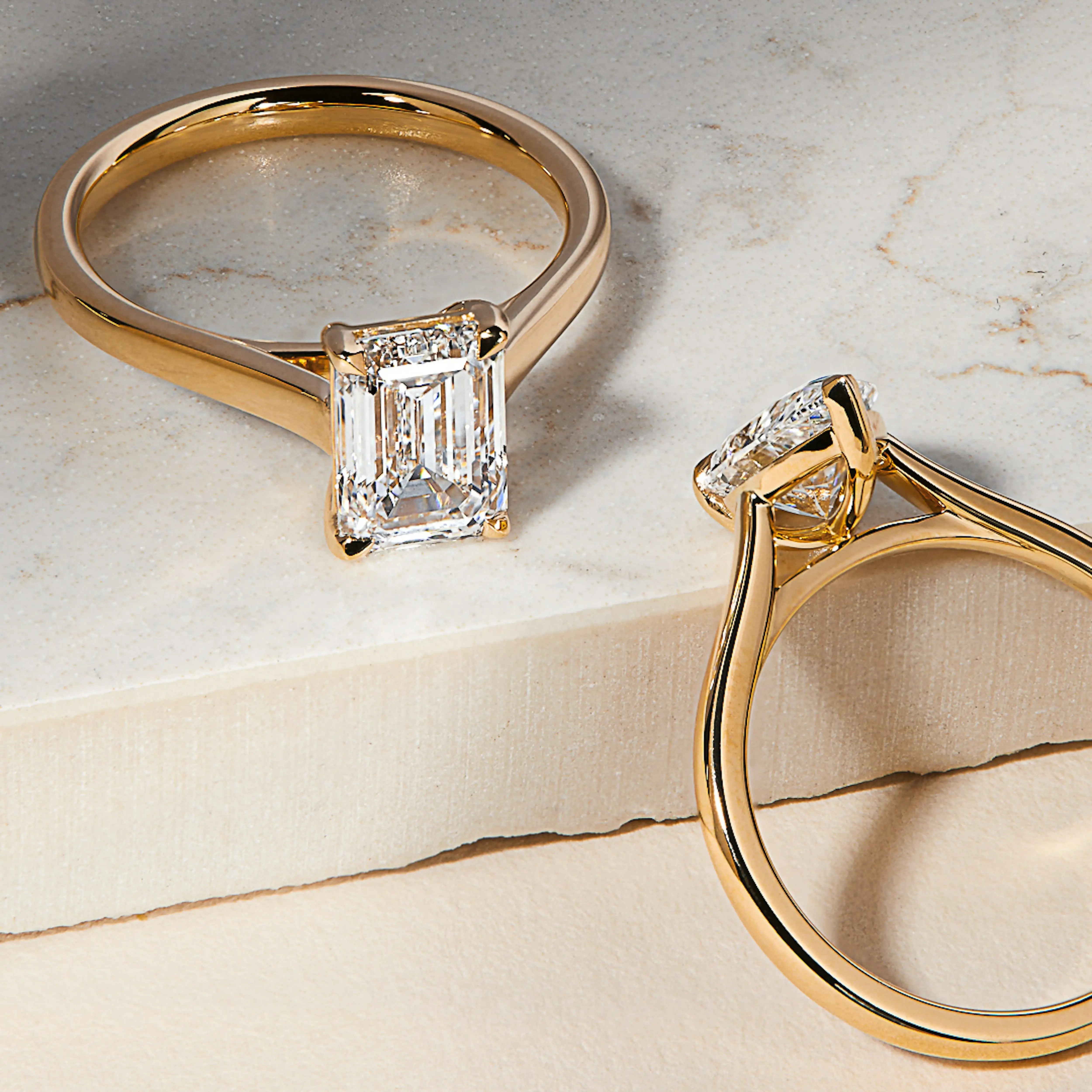 Two rose gold engagement rings with diamond accents on a marble surface
