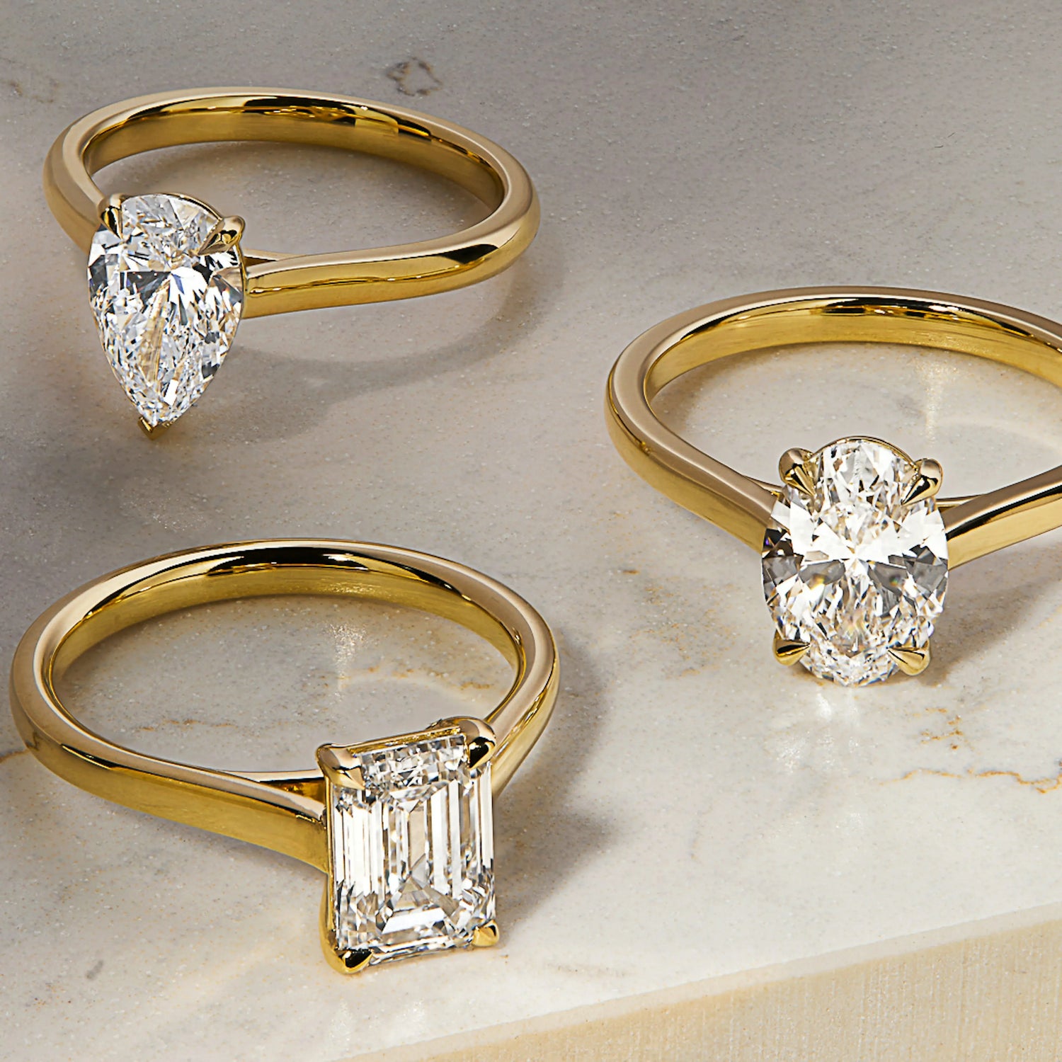 Three yellow gold rings with different diamond shapes on a light background