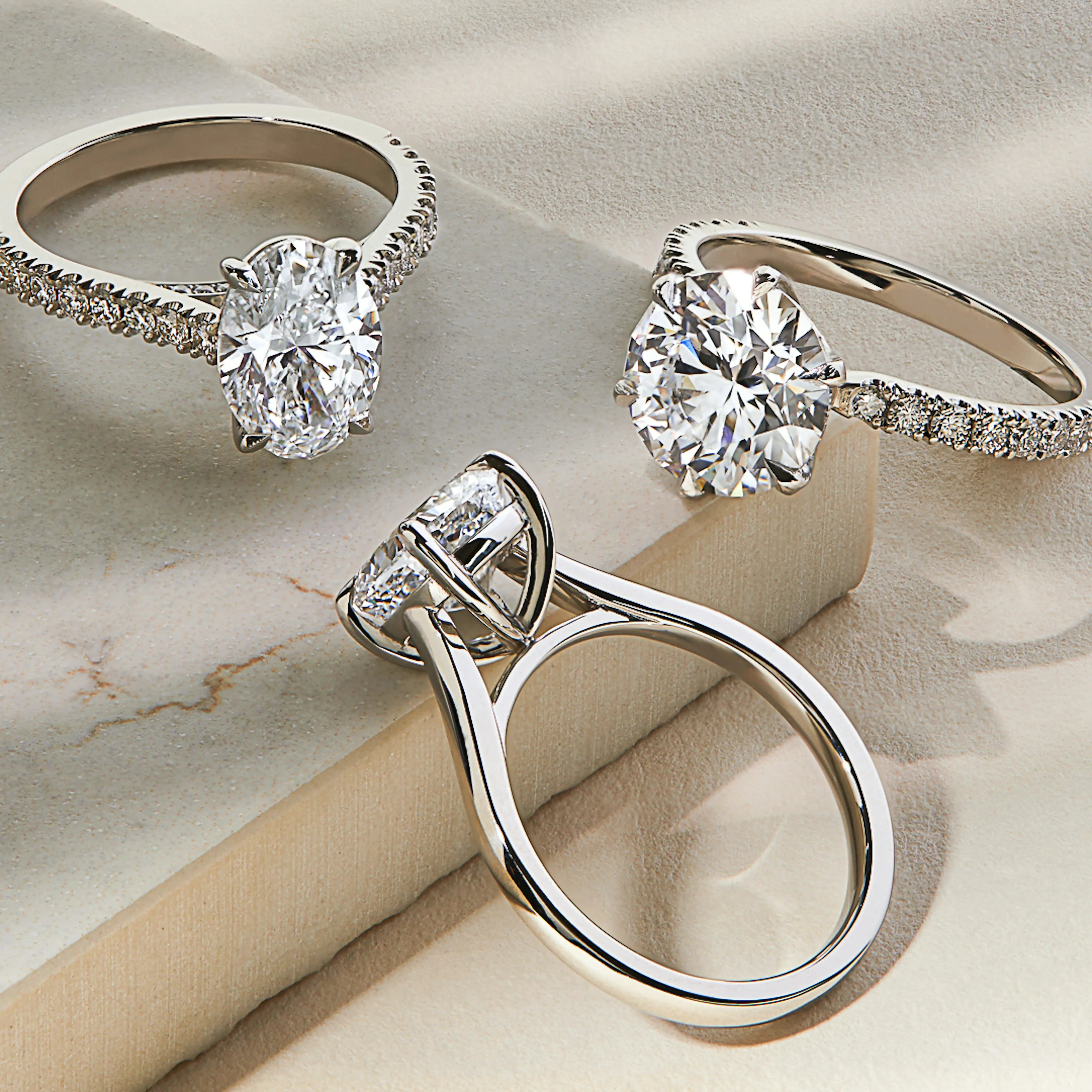 Three platinum lab-grown diamond engagement rings on a marble surface